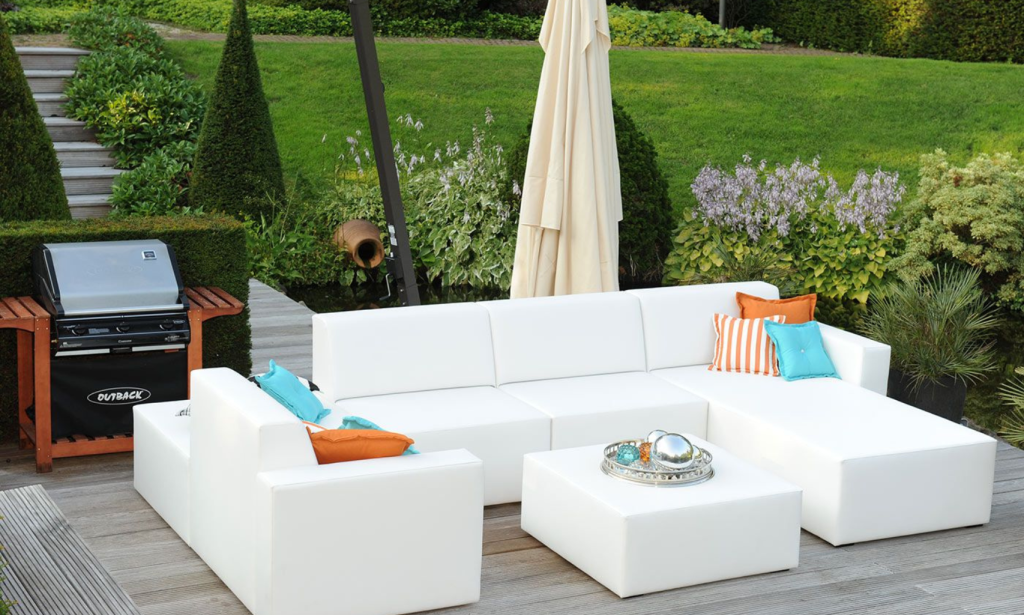 wiite loungeset met kussen en een hocker voor een groene tuin met een bbq