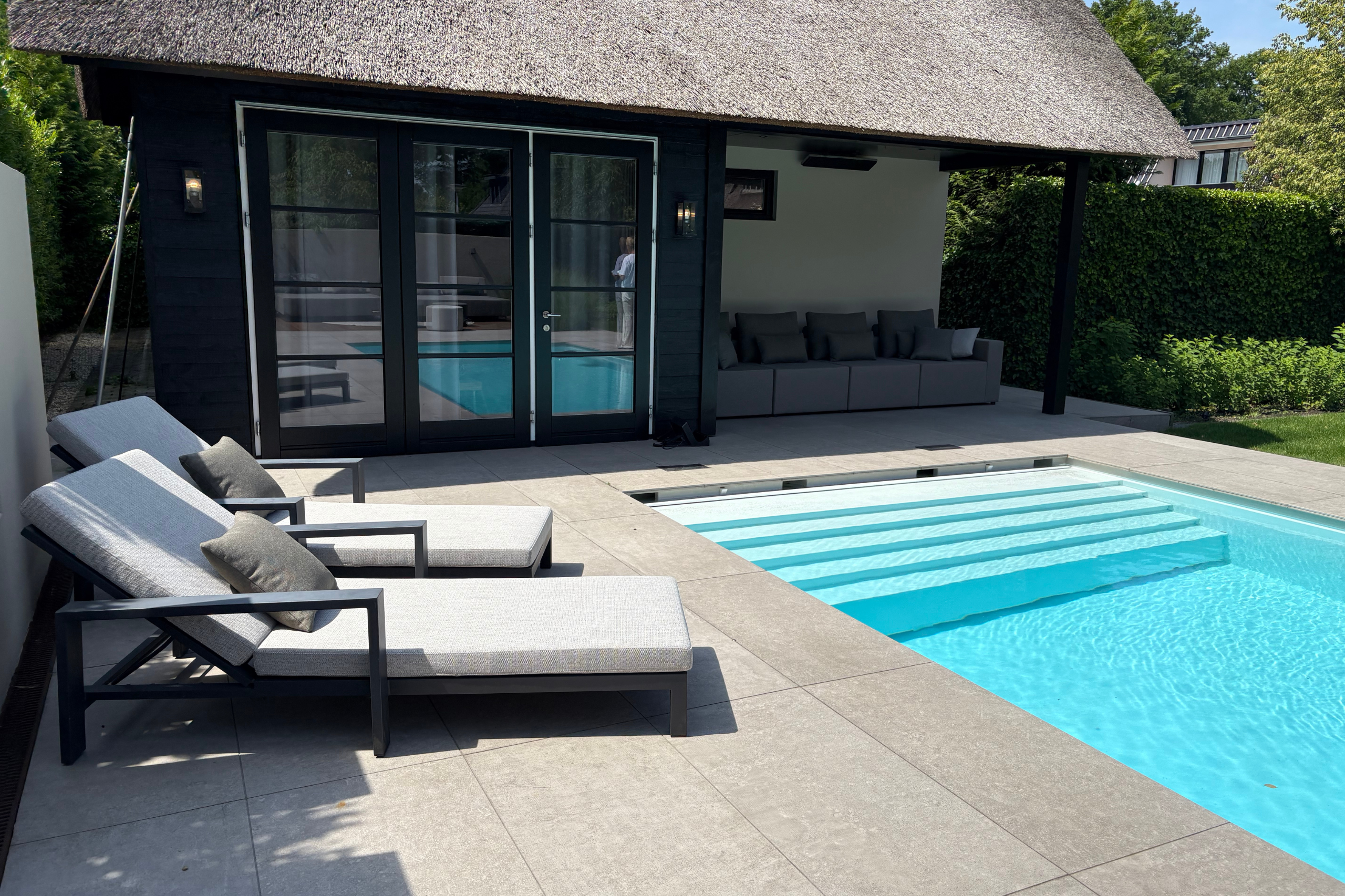 grijze ligstoelen aan een zwembad bij een huis