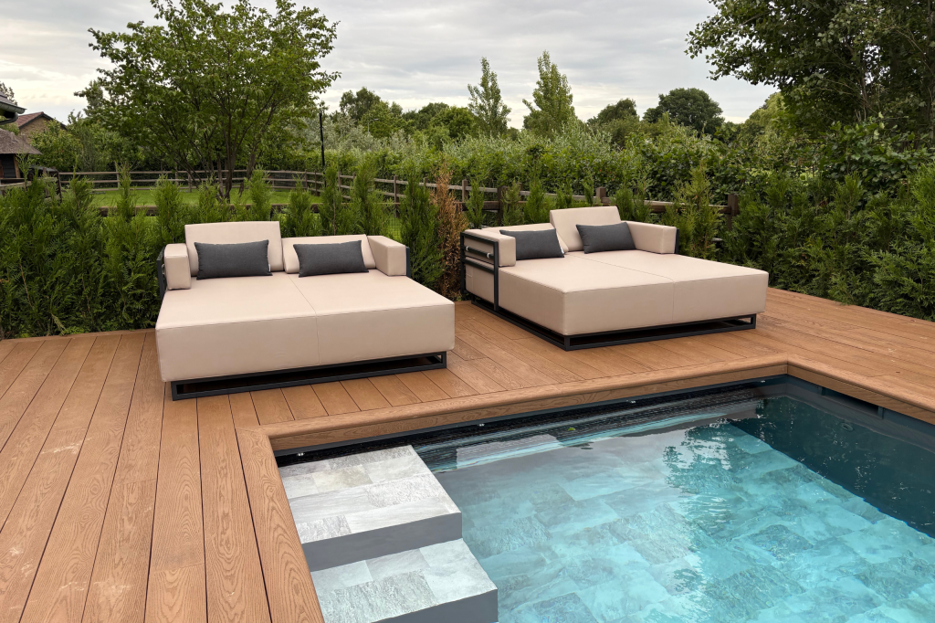 een beige lounge bed bij een zwembad met struiken vooraanzicht