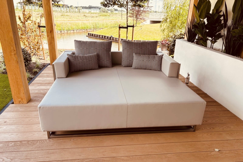 grijze lounge bed op een veranda langs een sloot